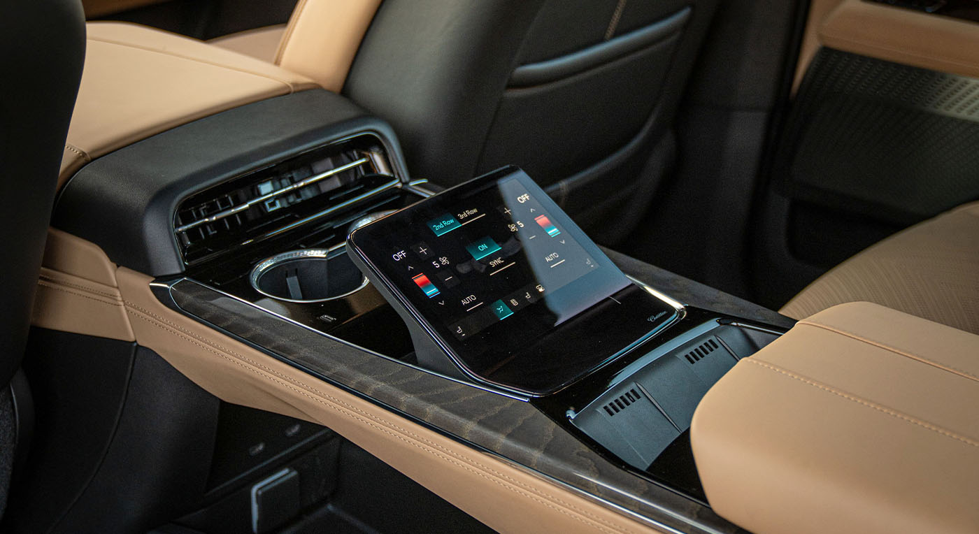 Luxury Cadillac Escalade IQ car interior with a sleek digital touchscreen on the center console, surrounded by beige leather seats. The mood is modern and sophisticated.